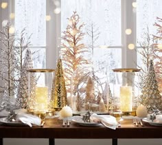 candles are sitting in glass vases with snow on the windowsill and christmas trees behind them