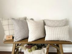 four pillows on a wooden bench in front of a white wall and wood flooring