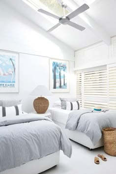 two beds in a room with white walls and ceiling fans above them, one has a blue striped comforter on the bed