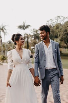 a man and woman holding hands while walking down a wooden walkway with palm trees in the background