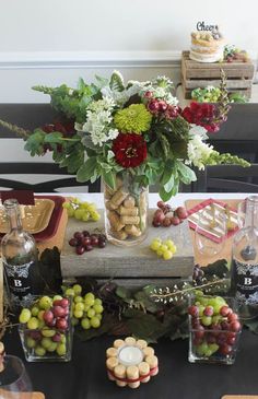 the table is set with grapes, flowers and wine bottles for an elegant centerpiece