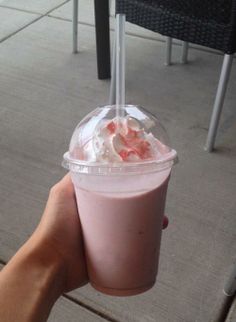 a hand holding up a pink drink with whipped cream and strawberries in it on a patio