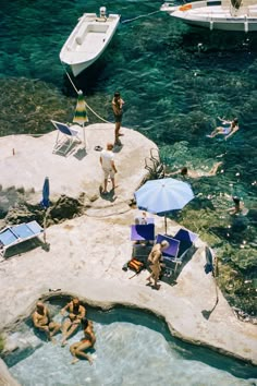 people are swimming in the clear blue water near boats and lounge chairs on an island