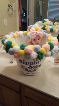 a baby is sitting in a bucket with pom poms on it's head