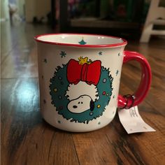 a red and white coffee cup with a christmas wreath on it sitting on a wooden table