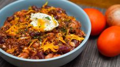 a blue bowl filled with chili and cheese next to two oranges on a table