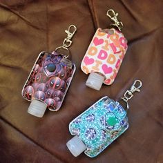 three bottle shaped key chains sitting on top of a brown leather surface with hearts and dots