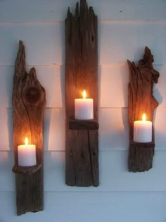 three candles are lit on the wall next to some driftwood pieces that have been placed together