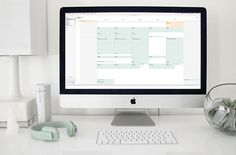 a desktop computer sitting on top of a white desk next to a vase with flowers