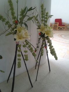 two vases filled with flowers on top of a white floor next to a wall