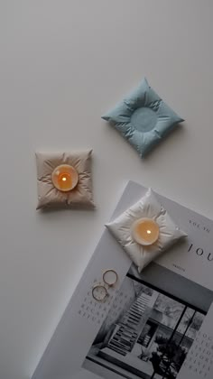 two candles are sitting on the table next to an open magazine and ring boxes with wedding rings