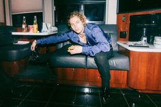 a man sitting on top of a black chair next to a counter in a kitchen