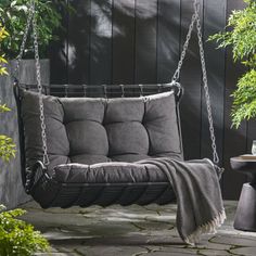 a swing chair with a blanket on it in the middle of a patio next to a potted plant