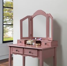 a pink dressing table with mirror and stool in front of a window on a hard wood floor