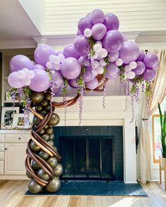 purple and white balloons are hanging from the ceiling above a fireplace in a living room