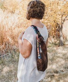 a woman standing in the grass with her back to the camera, wearing a bag