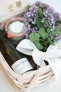 a white basket filled with bottles of wine and lavenders next to a bottle of wine