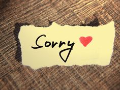 a torn piece of paper with the word sorry written on it and a red heart