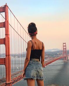 a woman standing in front of the golden gate bridge looking out at the water and hills