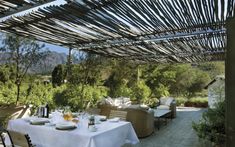 an outdoor dining area with white table cloths and wicker chairs, surrounded by greenery