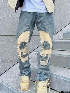 a man wearing ripped jeans with a skull on the side and one eye open, standing in front of some stairs