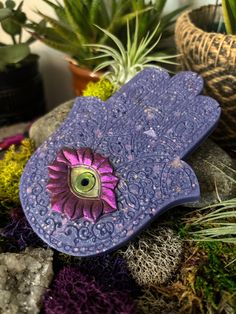 a purple flower sitting on top of a rock next to potted plants and rocks