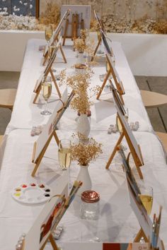 the table is set up with easels, paint brushes and flowers in vases