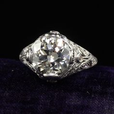 an old cut diamond ring with filigrees on the shoulders and sides, sitting on a purple velvet surface