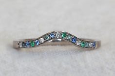 a white gold ring with blue, green and white stones on the side that is shaped like a wave