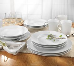 a table set with white plates, silverware and glasses on top of a wooden table