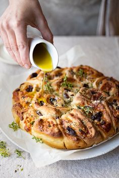 a person pouring olive oil on top of a pizza