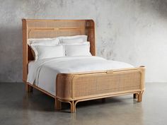 a wicker bed with white linens and pillows in a concrete walled bedroom area