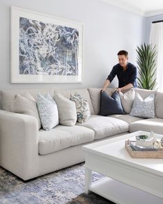 a man sitting on top of a white couch in a living room next to a window