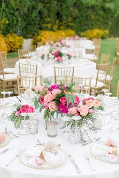 the centerpieces on this table are filled with pink roses and greenery, along with candles