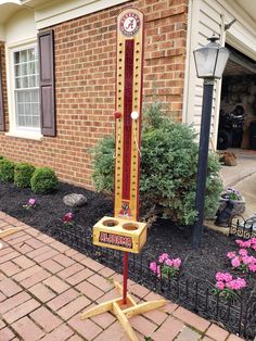 a clock on a pole in front of a brick building with flowers and bushes around it