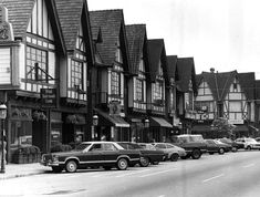 an old black and white photo of cars parked on the side of a street in front of buildings