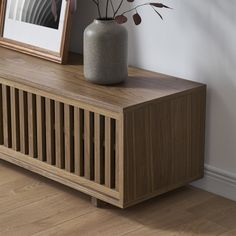 a vase sitting on top of a wooden cabinet next to a framed photo and plant