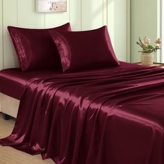 the bed is covered with burgundy sheets and pillow cases, along with a vase of flowers