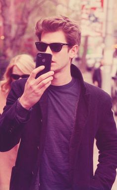 a man in black jacket and sunglasses looking at his cell phone while walking down the street