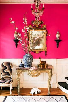 a room with pink walls and a table with flowers on it in front of a mirror