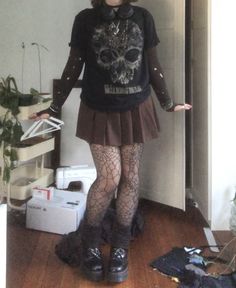 A mid-sized person/girl wearing a  black graphic skull t-shirt, a brown pleated skirt, a dark brown ripped tights long sleeve, dark brown legwarmers, black headphones, spider web tights, black platform dr. Martens and multiple dark green and gray crystal rings and bracelets. 		The person is also wearing multiple silver necklaces. Gremlincore Jewelry, Forest Gremlin, Earth Tones Outfit, Outfit Ideas Goth, Fashion Gender Neutral