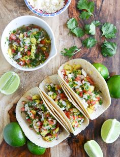 three tacos on a cutting board with limes and salsa