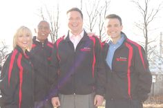 a group of people standing next to each other in front of trees and grass with one man smiling at the camera