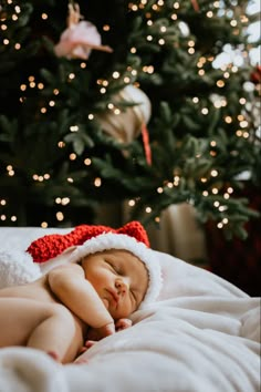 a baby is sleeping in front of a christmas tree wearing a red and white santa hat