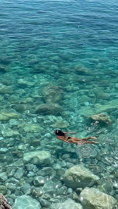 a woman swimming in clear blue water next to rocks