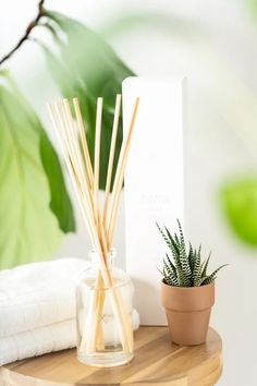 a wooden table topped with a potted plant next to a white towel and reed diffuser