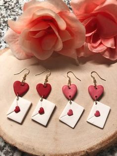 four heart shaped earrings are sitting on a piece of wood next to a rose and pink flower