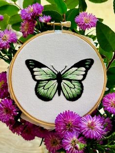 a close up of a embroidery on a hoop with flowers in front of it and a butterfly