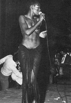 a black and white photo of a woman singing into a microphone while standing on stage