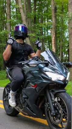 a man riding on the back of a black motorcycle down a street next to trees